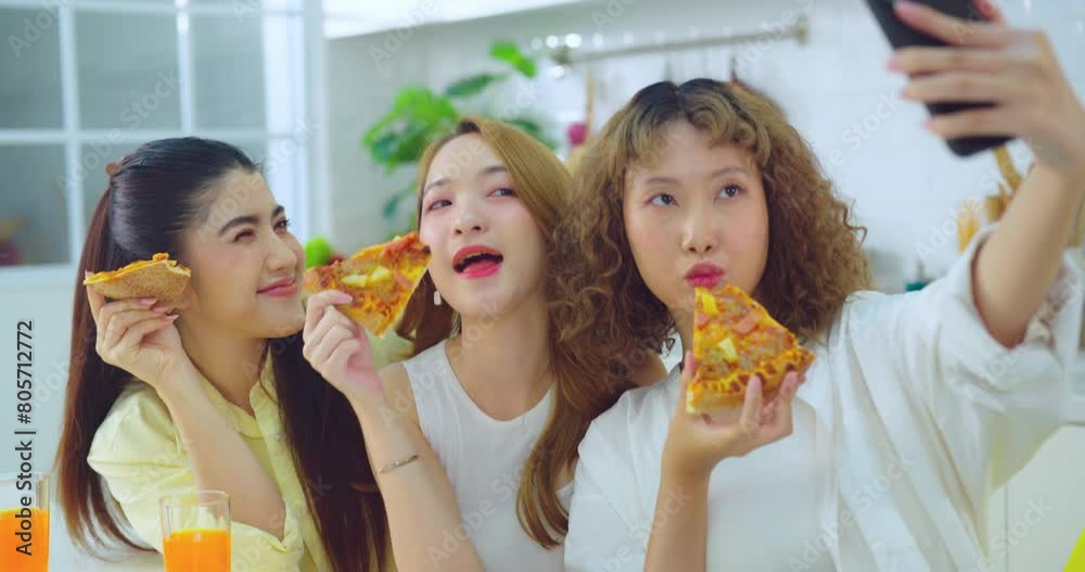 Three young women enjoy slices of pizza and take a selfie in a bright, modern kitchen setting. Three young women enjoy slices of pizza and take a selfie in a bright, modern kitchen setting.