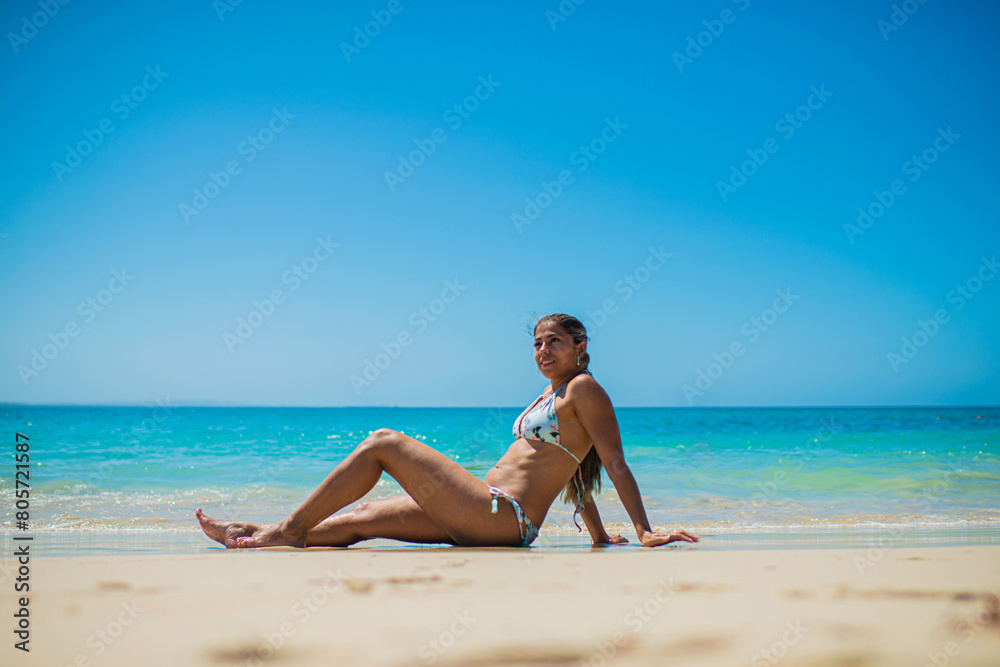 mujer hispano americana en la playa tomando el sol sentada en la arena a orilla del mar en vacaciones 