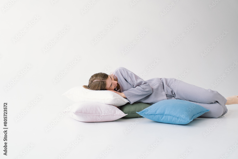 A woman lies comfortably on her side, embracing a white pillow with a tranquil expression. She is wearing a pajamas and resting against a light, solid-colored backdrop, evoking a sense of relaxation A woman lies comfortably on her side, embracing a white pillow with a tranquil expression. She is wearing a pajamas and resting against a light, solid-colored backdrop, evoking a sense of relaxation