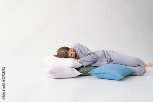 A woman lies comfortably on her side, embracing a white pillow with a tranquil expression. She is wearing a pajamas and resting against a light, solid-colored backdrop, evoking a sense of relaxation