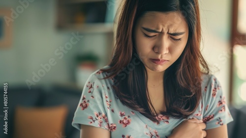 Asian woman with a pained expression, holding her stomach in discomfort. abdominal pain photo
