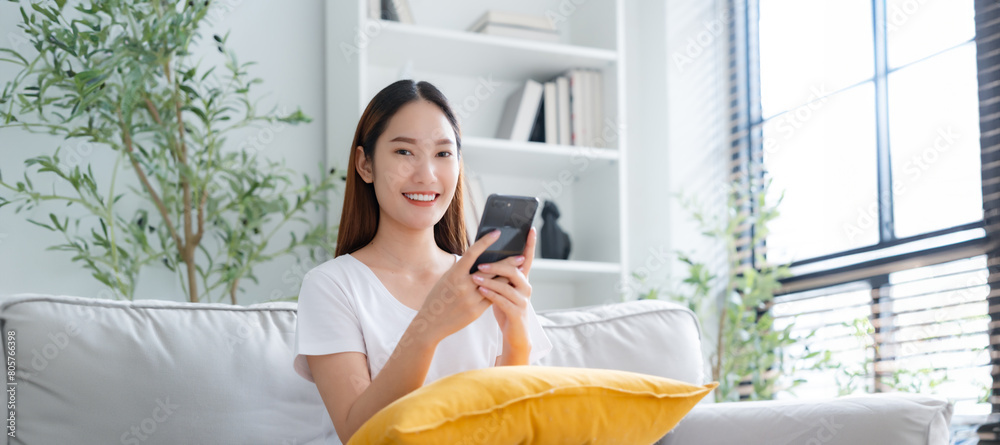 Happy young Asian woman relax sitting on couch using cell phone ...
