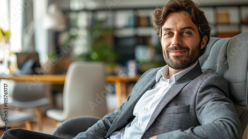 Portrait of handsome businessman sitting on armchair in office and looking at camera