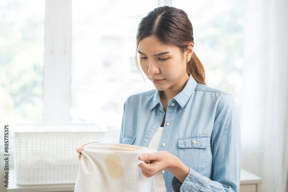 Dirty coffee stain cloth, housewife asian young woman holding white shirt, showing making cloth stain, spot dirty or smudge on clothes for cleaning before washing, maid female working at home concept Dirty coffee stain cloth, housewife asian young woman holding white shirt, showing making cloth stain, spot dirty or smudge on clothes for cleaning before washing, maid female working at home concept