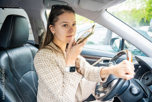 Young woman sending a voice message with mobile phone inside the car