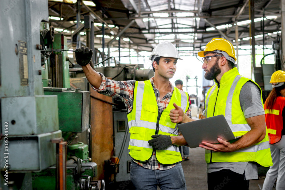 Industrial foreman and worker with helmet and safety vest using laptop computer during discussing together at manufacturing industry factory. Engineer inspecting workplace and checking process. Industrial foreman and worker with helmet and safety vest using laptop computer during discussing together at manufacturing industry factory. Engineer inspecting workplace and checking process.