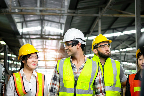Group of industrial foreman engineer and workers with helmet and safety vest walking past to inspect machinery engine and production process at manufacturing industry factory. Teamwork at workplace