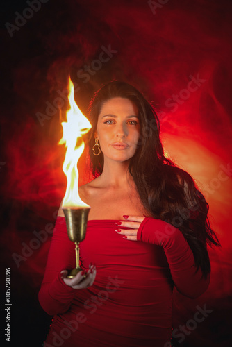 Young beautiful girl with dark hair and in the red dress posing in the dark background with the fire. photo