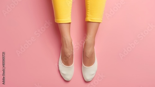  A tight shot of legs clad in yellow trousers and white sneakers, against a pink backdrop wall photo