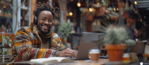 Smiling African American student outdoors with laptop, surrounded by plants, wearing winter clothing photo