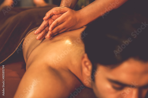 Caucasian man customer enjoying relaxing anti-stress spa massage and pampering with beauty skin recreation leisure in warm candle lighting ambient salon spa at luxury resort or hotel. Quiescent