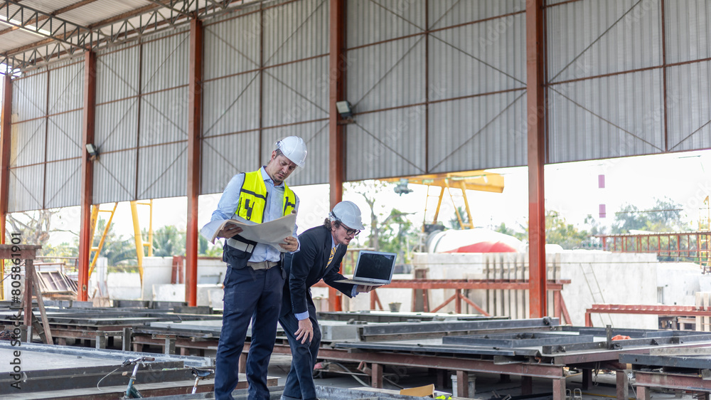 Two manufacturing engineers using computer notebook to check production system in construction factory. Factory owner and his civil engineer using laptop to design production and management systems.