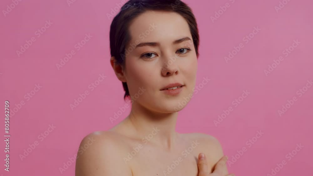 Young beautiful woman with clean skin touching her shoulder and looking at the camera on a pink background close up. Concept of skin care for health and beauty Young beautiful woman with clean skin touching her shoulder and looking at the camera on a pink background close up. Concept of skin care for health and beauty