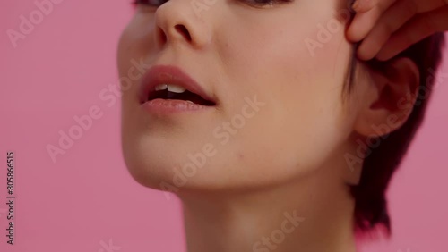 Young attractive woman with clean skin touching her face by the hand close up and coquettishly looking at the camera on a pink background. Concept of skin care for health and beauty photo