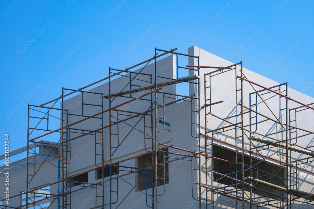 Scaffolding on concrete wall outside of office building structure against blue clear sky background Scaffolding on concrete wall outside of office building structure against blue clear sky background