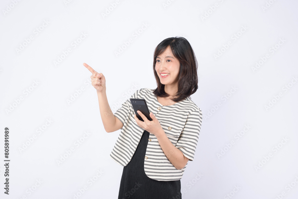 Asian woman is holding a mobile phone and pointing to an empty space on a white background. Asian woman is holding a mobile phone and pointing to an empty space on a white background.
