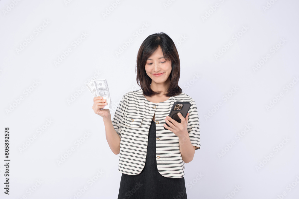 Asian woman is holding dollar and a mobile phone against a white background, concept of mobile banking. Asian woman is holding dollar and a mobile phone against a white background, concept of mobile banking.