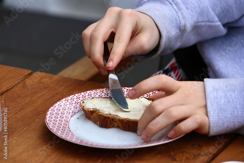 Kind schmiert Brut mit Butter. Frau schmiert ein Butterbrot mit dem Messer photo