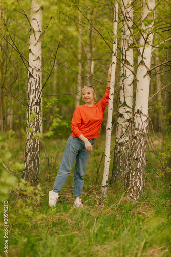 a girl in blue jeans and an orange jumper among birch trees, taken on a cloudy spring day in the village of Shanary in Chuvashia