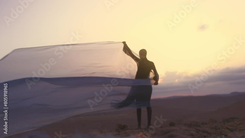 Model with shaved head holding a silk sheet in the wind in desert