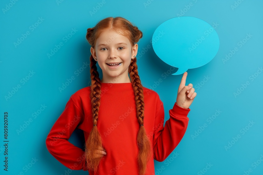 Girl holding speech bubble above her head isolated on blue background, pointing finger at it Girl holding speech bubble above her head isolated on blue background, pointing finger at it