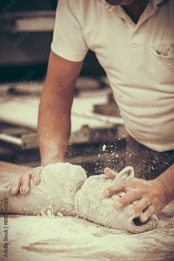 A baker kneads bread dough in the bakery. Vintage style with grain. Vertical.