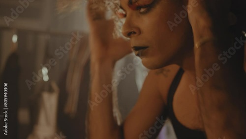 Drag queen tucks in strands of hair into wig in dressing room