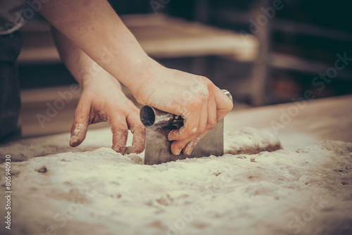 A female baker divides pieces of dough with a dough cutter. Vintage style with grain.