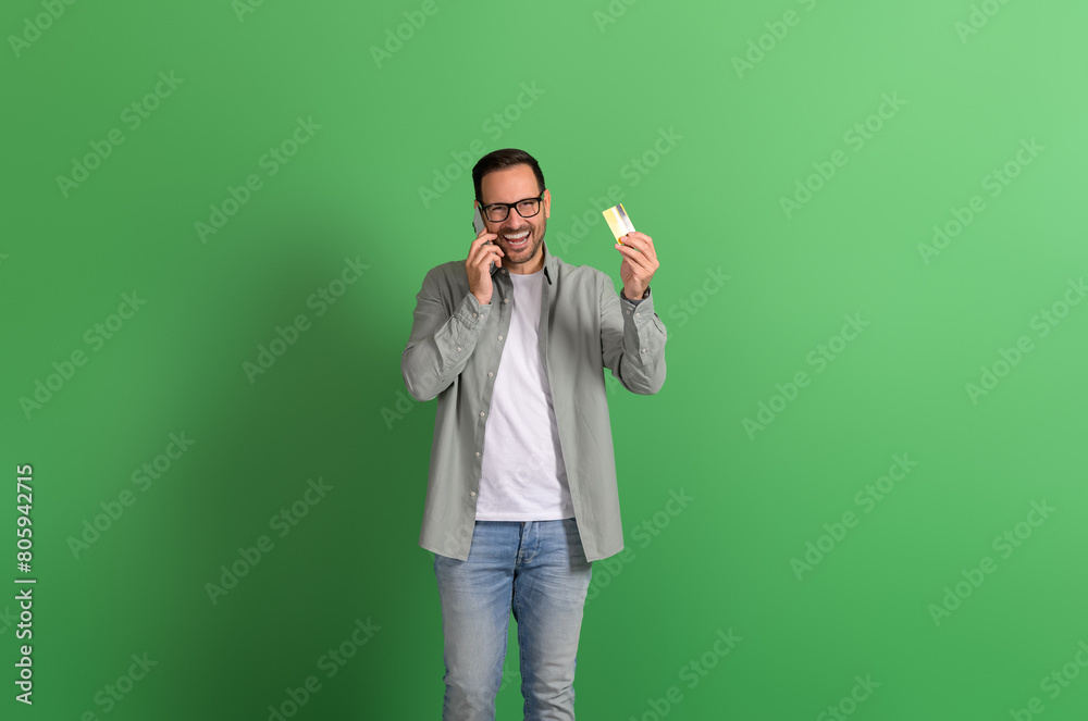 Portrait of happy businessman talking on mobile phone and showing credit card over green background Portrait of happy businessman talking on mobile phone and showing credit card over green background