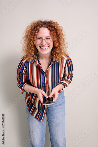 Portrait of cheerful businesswoman with curly redhead texting over smartphone on white background