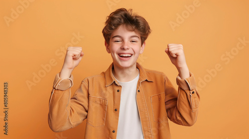 Young happy very excited funny teenage boy in casual clothes do winner gesture clenching his fists celebrating success isolated on studio beige background with copy space. People emotions concept