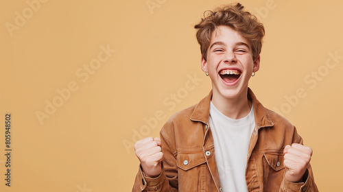 Young happy very excited funny teenage boy in casual clothes do winner gesture clenching his fists celebrating success isolated on studio beige background with copy space. People emotions concept