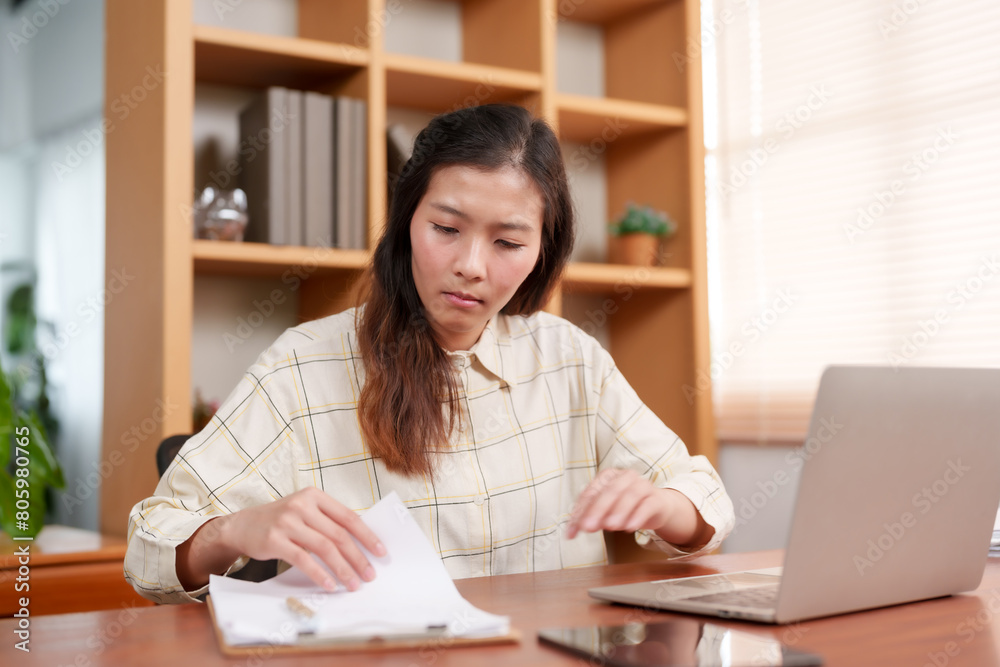 Office employee reviewing documents with a focused expression, suggesting careful analysis or scrutiny of paperwork.  Office workers are working