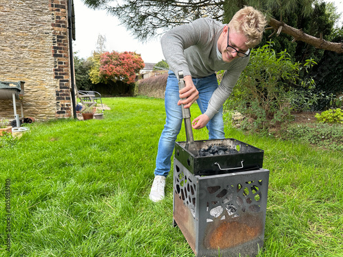 Full length shot of a handsome young man starting fire in a small portable grill in his garden