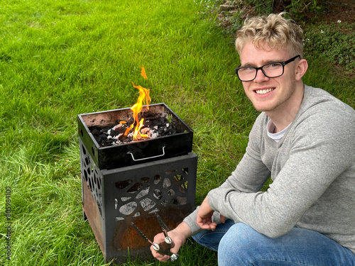 Happy handsome man smiling to the camera while starting a fire in a bbq grill pit