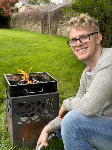Cheerful young man smiling to the camera while preparing grill pit for a garden party