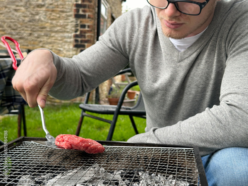Cropped shot of a man putting burgers on a small grill in his garden