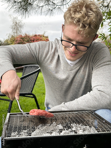 Young happy man putting burgers on a grill