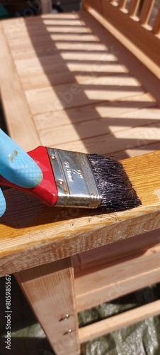 Painting a wooden bench outdoors with wood preservative using blue rubber gloves
