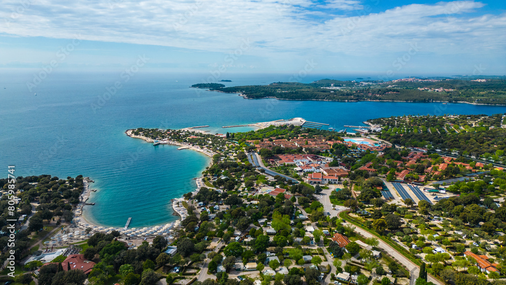 Camp Valalta reveals its expansive grounds, nestled between lush greenery and the crystal-clear waters of the Adriatic Sea captured by drone