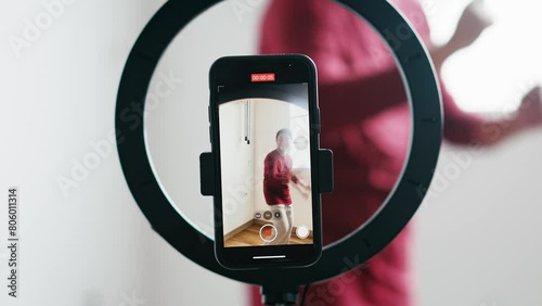 Selective Focus Smartphone and Ringlight Recording Attractive Young Man Dancing, Live Streaming on Social Media Platform 