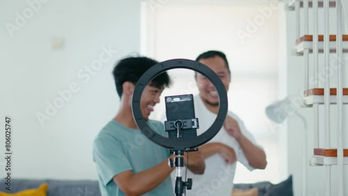 Selective Focus Smartphone and Ringlight Recording Attractive Two Young Man Dancing, Live Streaming on Social Media Platform  photo