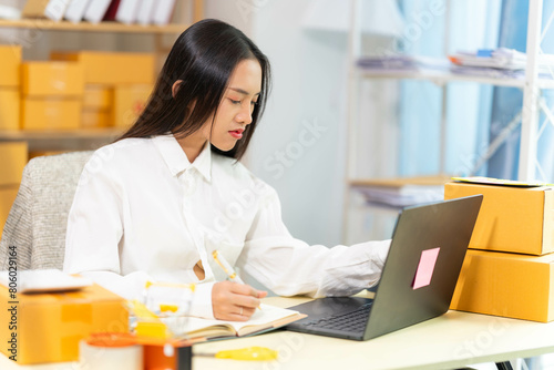  woman sit at workplace desk laughing working on-line using laptop in warehouse. 