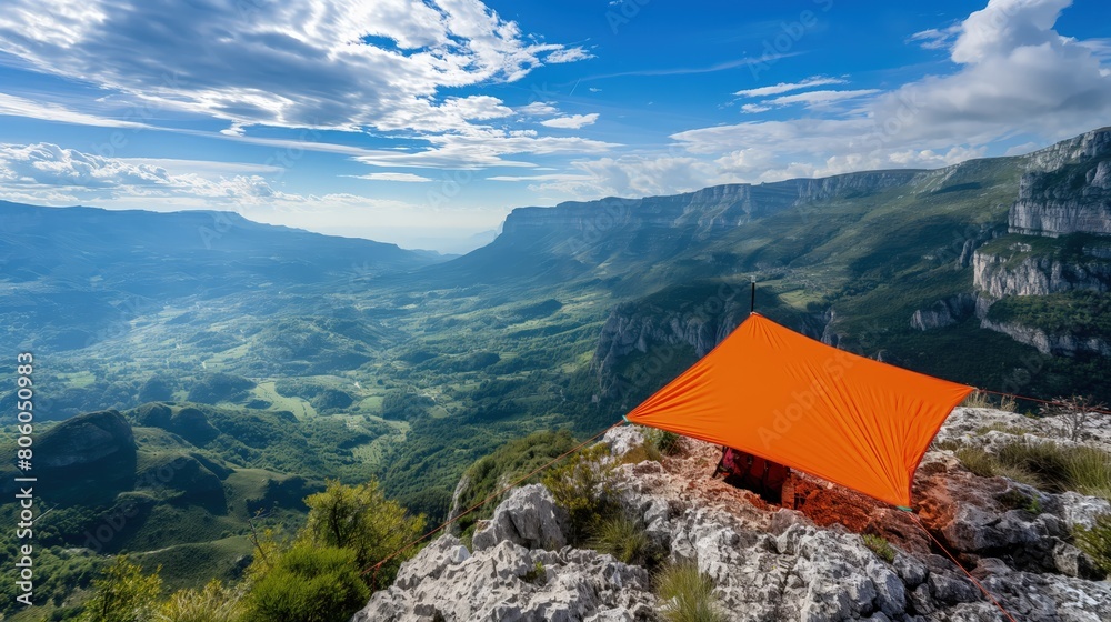Obraz premium A compact, foldable sunshade in bright orange, set up on a rocky mountain overlook with a panoramic view of the valley below.