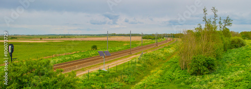 Railroad track in a green field in wetland below a blue cloudy sky in springtime, Almere, Flevoland, The Netherlands, May 4, 2024