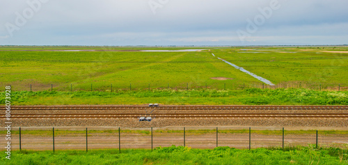 Railroad track in a green field in wetland below a blue cloudy sky in springtime, Almere, Flevoland, The Netherlands, May 4, 2024