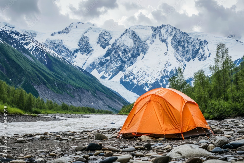 A bright tent on the river bank against the backdrop of the mountains. Concept of tourism, vacation, travel, hiking