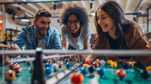 Positive excited young multiethnic couple of professionals playing toy football, competing in table soccer with coworkers, turning handles at field miniature, laughing, relaxing on work break photo