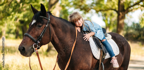 Cute little girl with long hair riding a horse outdoors. Pet therapy