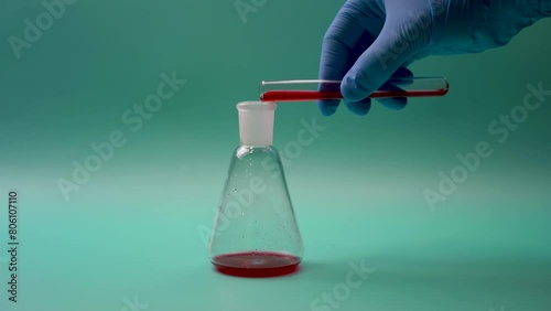 Hand of anonymous medical scientist in disposable glove pouring red liquid sample from test tube into titration flask during science laboratory research photo